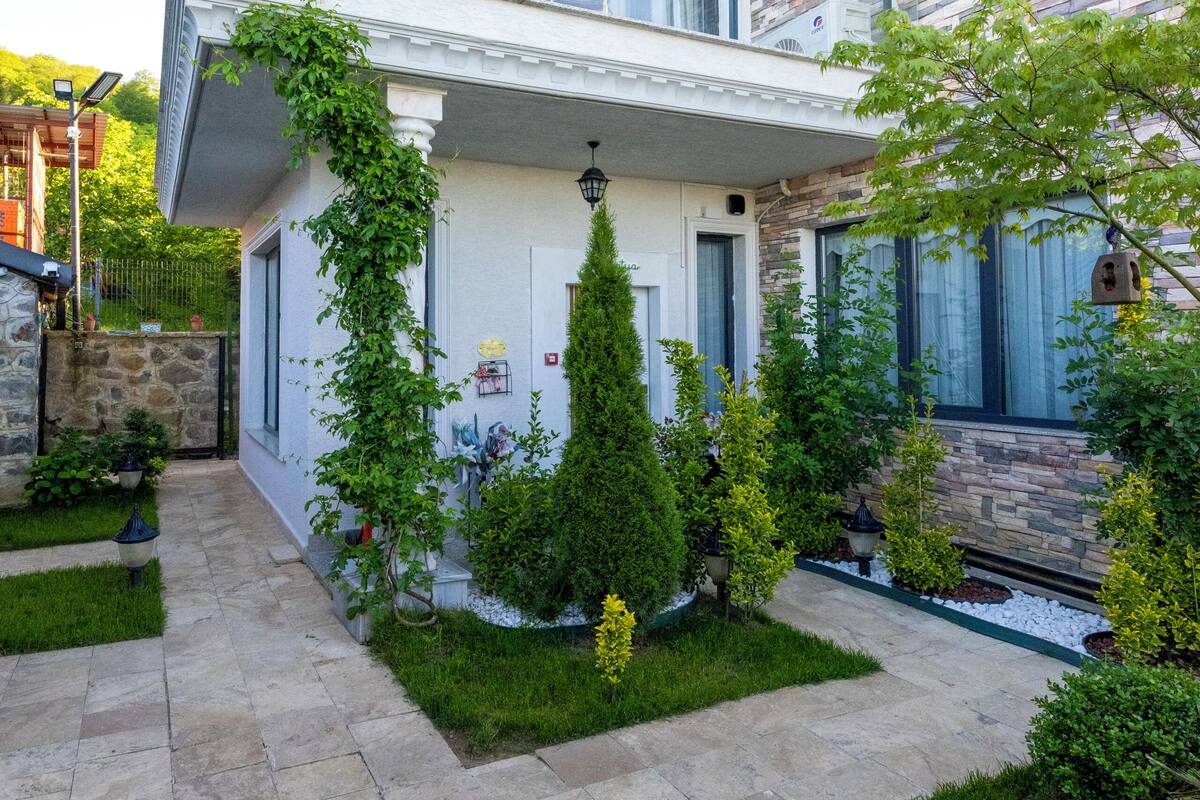 A two-story house with a stone facade, a balcony, and a well-maintained garden.