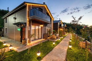 A modern two-story house with a stone pathway, outdoor seating, and decorative lighting. - Poison Garden Suite & SPA (Trabzon)