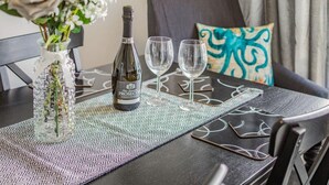 A dining table with a bottle of wine, two glasses, and a vase with flowers. - Lovely Apartment 3 King-size Beds (Torquay)