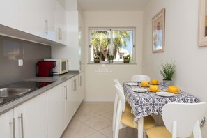 Une cuisine avec des meubles blancs, un appareil électroménager rouge et un coin repas avec une table mise pour quatre personnes.