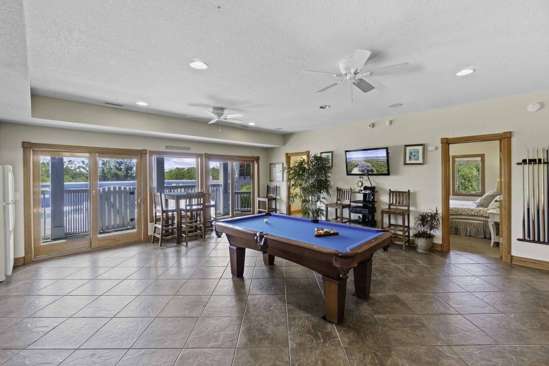 A pool table in a spacious room with a ceiling fan, a television, and a view of the outdoors.