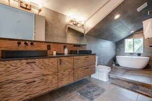 Un baño moderno con tocador de madera, un espejo grande, una bañera independiente y un inodoro.