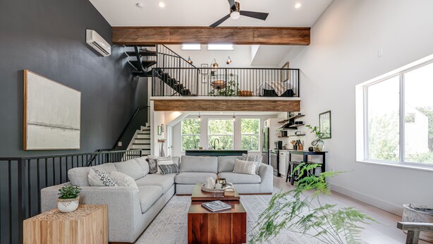A spacious living room with a grey sectional sofa, a wooden coffee table, and a staircase leading to an upper level.