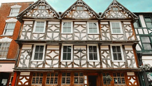 A traditional half-timbered building with a symmetrical facade, large windows, and a central entrance.