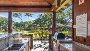 An outdoor kitchen with a stone countertop, stainless steel sink, and a grill.