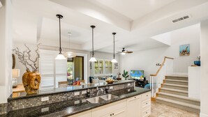A spacious kitchen with a large island, pendant lighting, and a view to the living area.