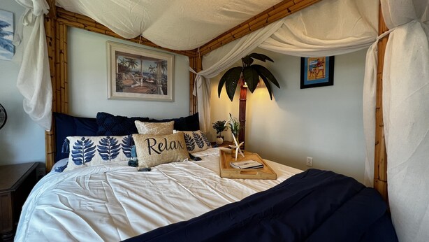 Ein Schlafzimmer mit Baldachinbett, Nachttisch mit Lampe und einem gerahmten Bild an der Wand.