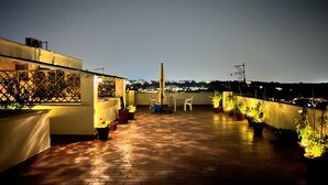 Una terrazza sul tetto con piante in vaso, mobili da esterno e vista sulla città di notte.