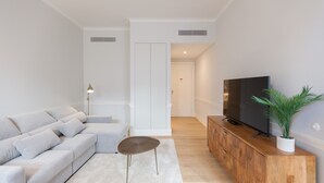 A modern living room with a grey sofa, a small round table, a wooden cabinet with a TV, and a potted plant. - FLH Praça Rossio Elegant Flat (Lisbon)