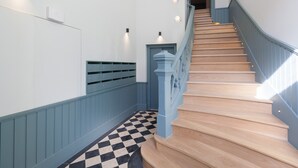 A staircase with wooden steps and blue railings, leading to a landing with a checkered floor and a light fixture on the wall. - FLH Praça Rossio Elegant Flat (Lisbon)