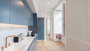 A modern kitchen with a long countertop, built-in cabinets, and a wooden floor. - FLH Praça Rossio Elegant Flat (Lisbon)