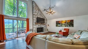 A spacious living room with a stone fireplace, a large sofa, a red armchair, and a view of a deck with outdoor furniture.