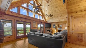 A cozy cabin interior with a leather sofa, a fireplace, and a large window overlooking a scenic landscape. - 🌄Sleeps up to 16 🌄 Pristine Mountain Views from Downtown Helen ⛰️ (Helen)