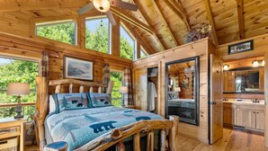 A log cabin bedroom with a bed, a wooden headboard, a large window, and a view of the outdoors. - 🌄Sleeps up to 16 🌄 Pristine Mountain Views from Downtown Helen ⛰️ (Helen)