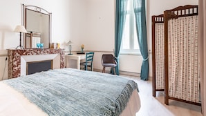 Een slaapkamer met een bed, een bureau, een stoel, een spiegel en een raam met gordijnen.