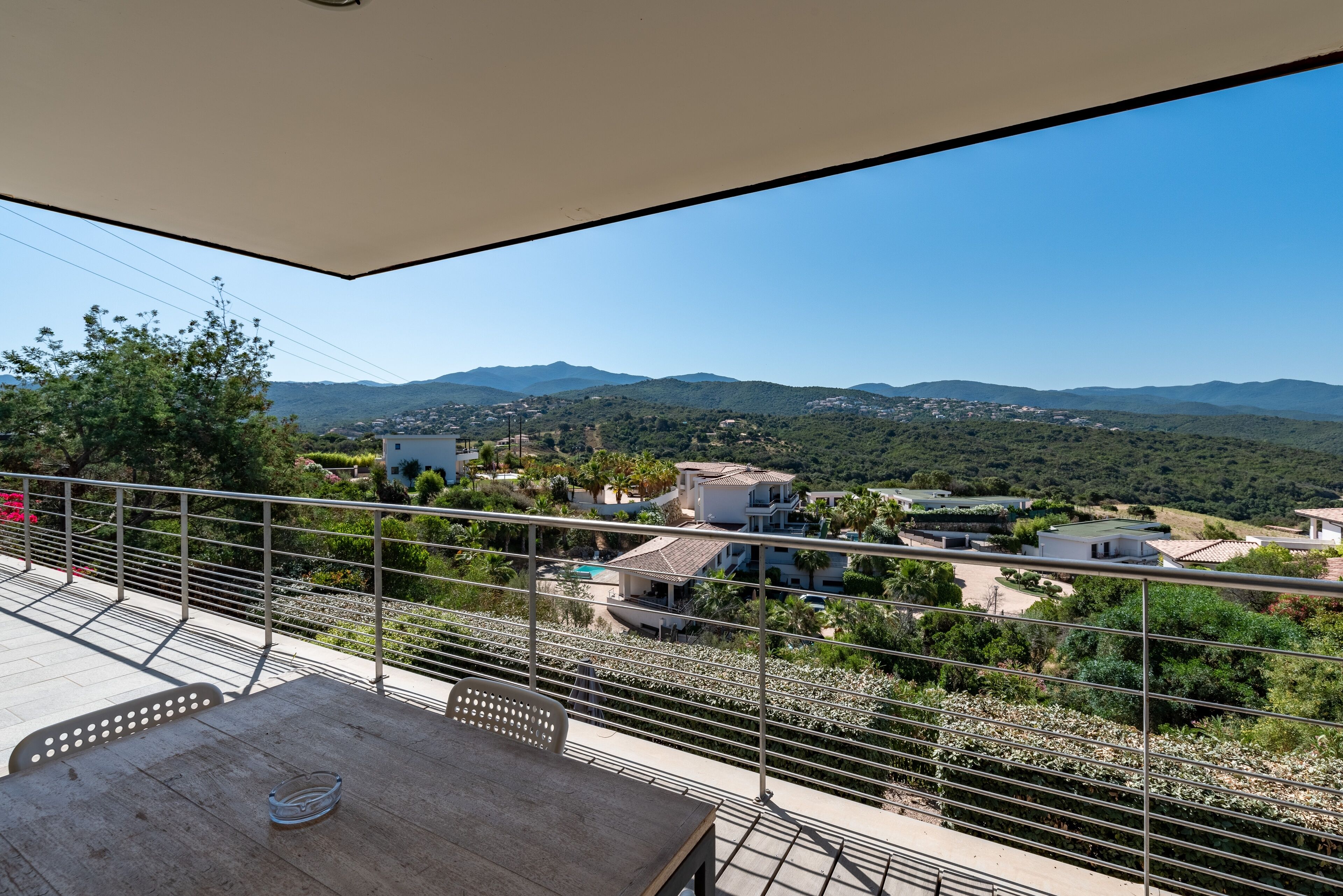 A balcony with a view of a mountainous landscape, a table, and chairs.
