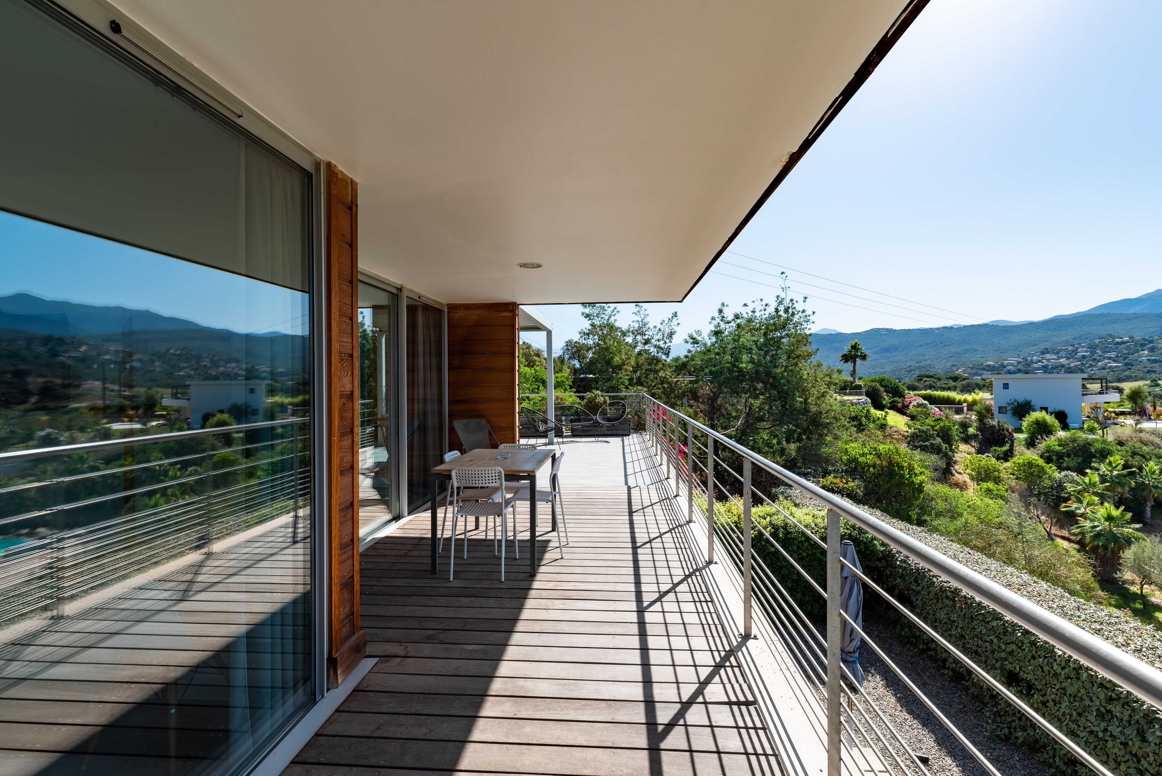 A balcony with a table and chairs, overlooking a scenic landscape with mountains and a lake.