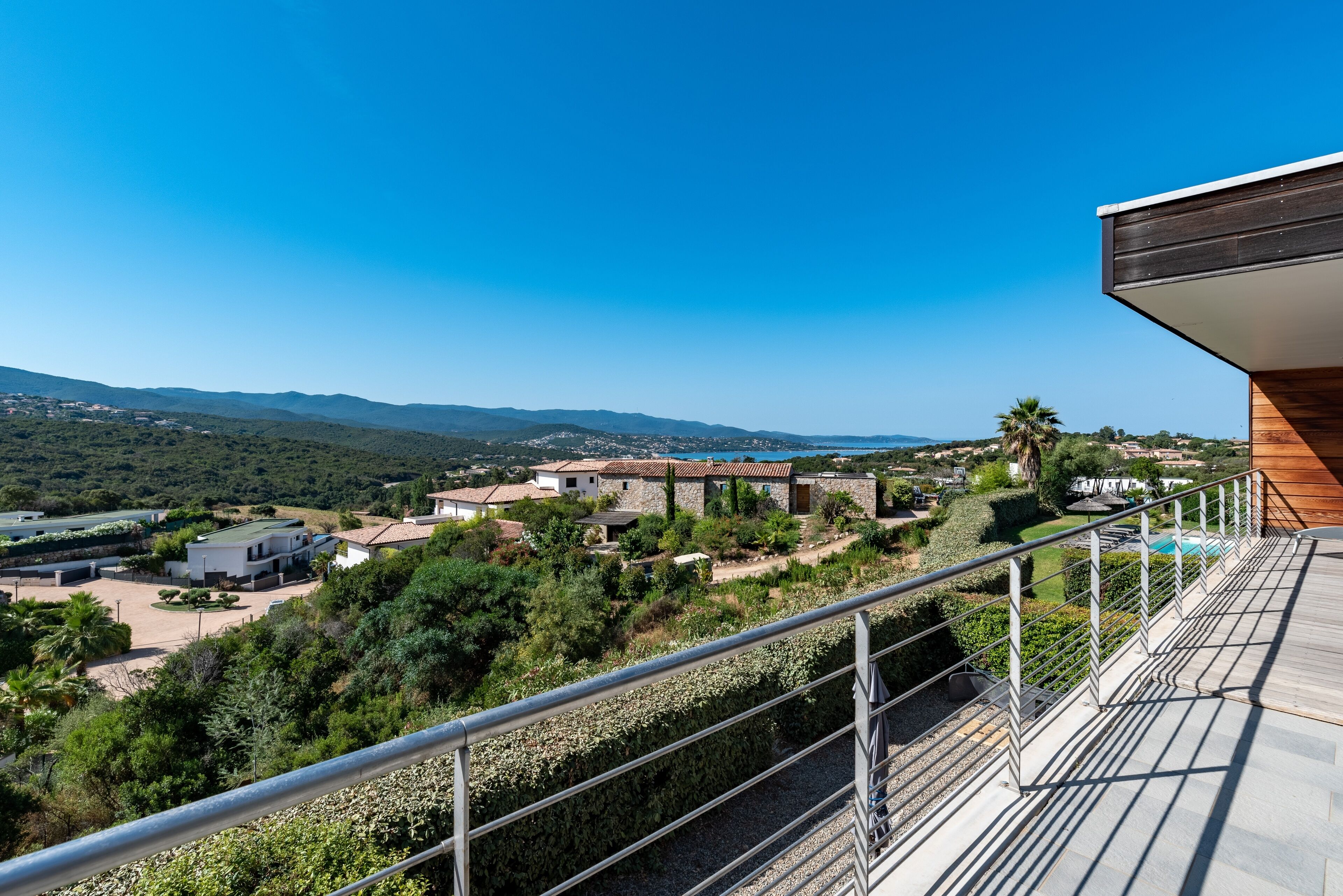 A balcony with a metal railing overlooking a residential area with houses and greenery.