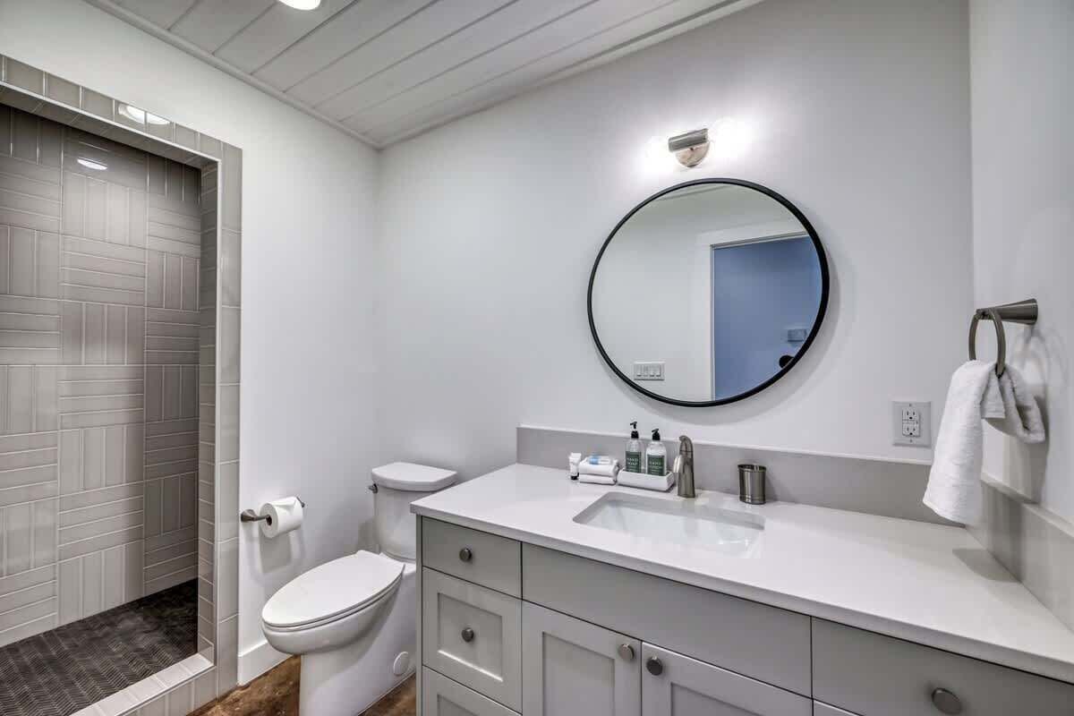 A modern bathroom with a white vanity, a round mirror, and a toilet.