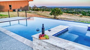 Una piscina infinita con borde de mármol, una bandeja de frutas y vino, y vistas a un paisaje montañoso.