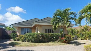 A single-story house with a tiled driveway, surrounded by well-maintained hedges and palm trees. - Cozy 3-Bedroom Vacation Home (Richmond Estates)