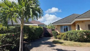 A residential area with a paved pathway, a palm tree, and houses with sloped roofs. - Cozy 3-Bedroom Vacation Home (Richmond Estates)