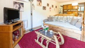 Un salon chaleureux avec un canapé en bois, un téléviseur posé sur un meuble en bois et un tapis rouge à longues mèches.