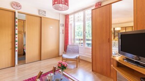 Un salon avec des meubles en bois, un téléviseur, un fauteuil et une table sur laquelle est posé un vase de fleurs.