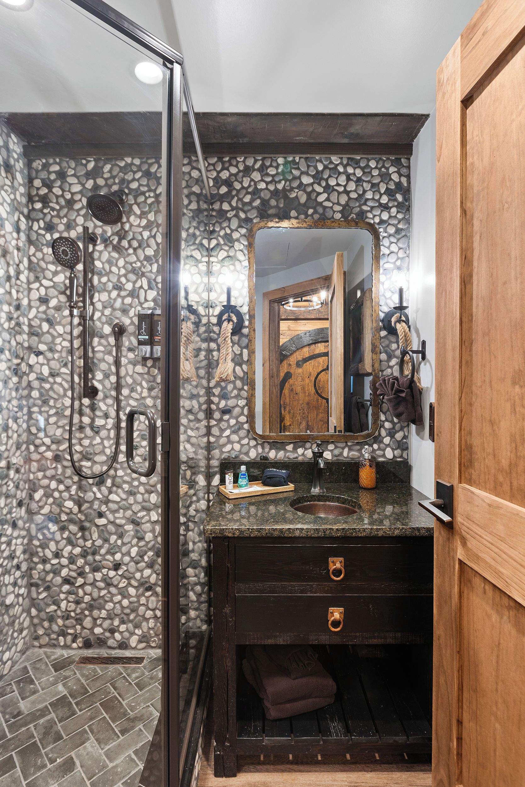 Un baño con pared de piedra, tocador de madera, cabina de ducha de vidrio y espejo con marco de madera.
