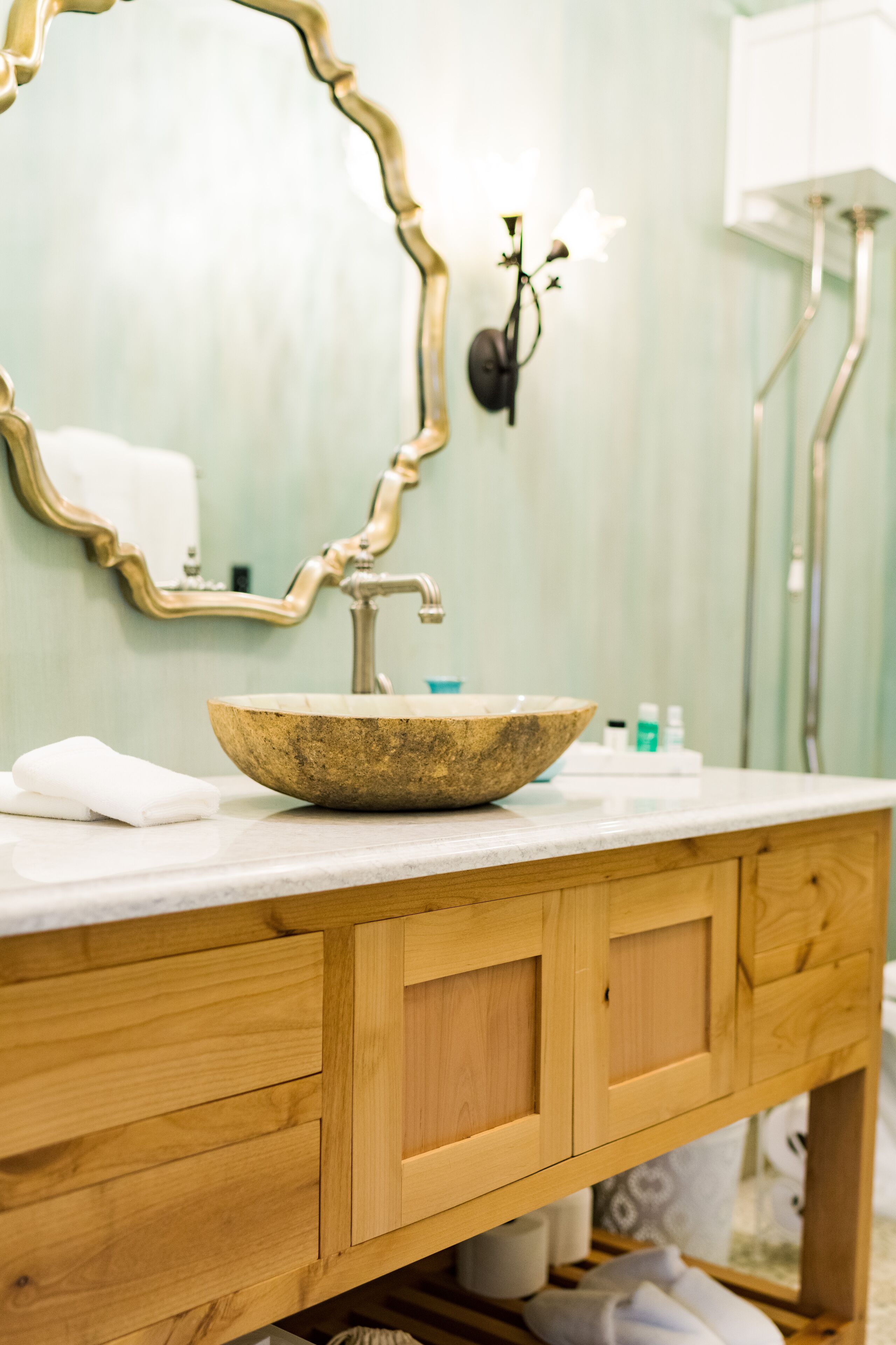 A bathroom with a wooden vanity, a large mirror, a vessel sink, and a wall-mounted light fixture.