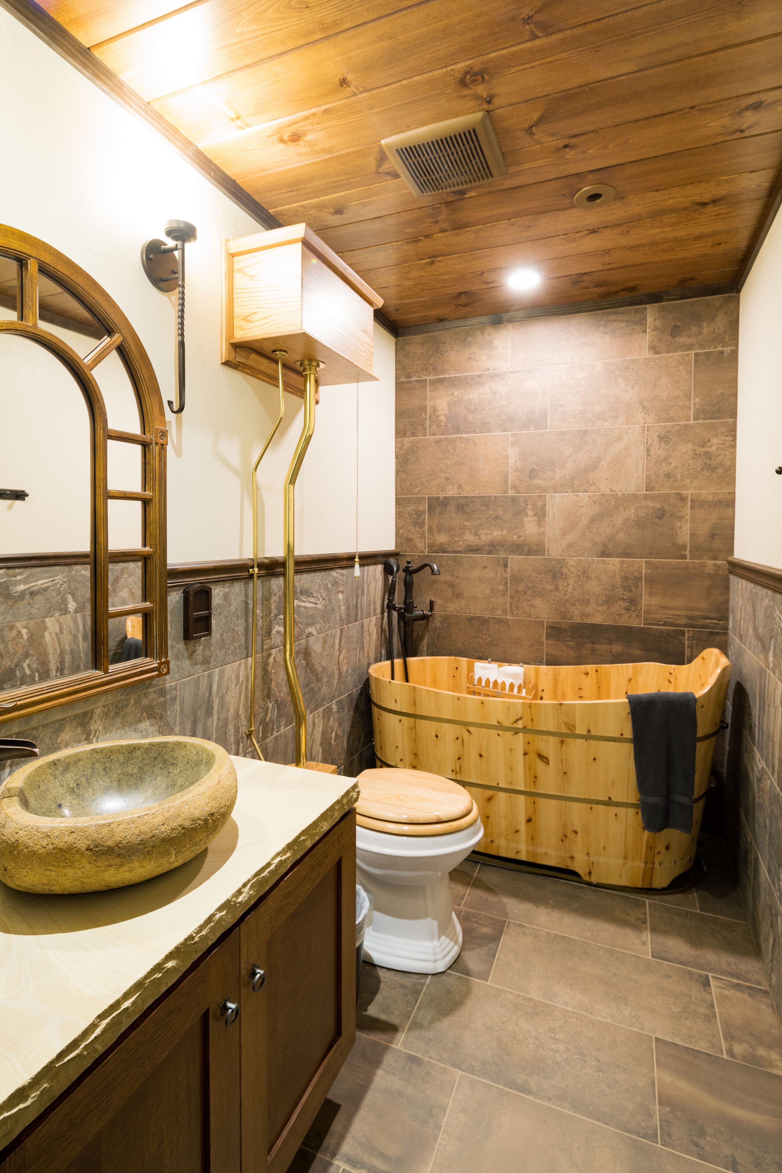 A bathroom with a wooden bathtub, a stone sink, and a wooden vanity.