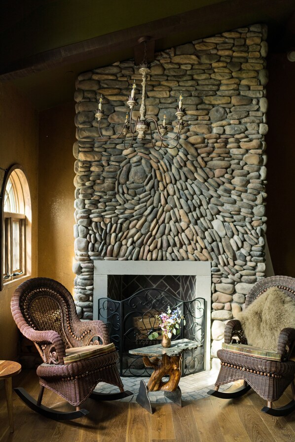 A cozy room with a stone wall, a fireplace, wicker rocking chairs, and a chandelier.