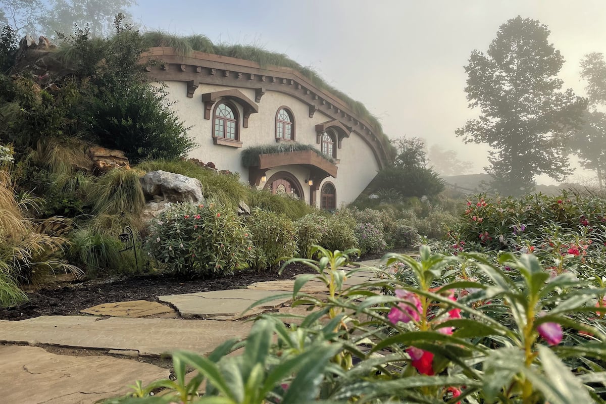A house with a unique curved roof, surrounded by lush greenery and flowering plants.