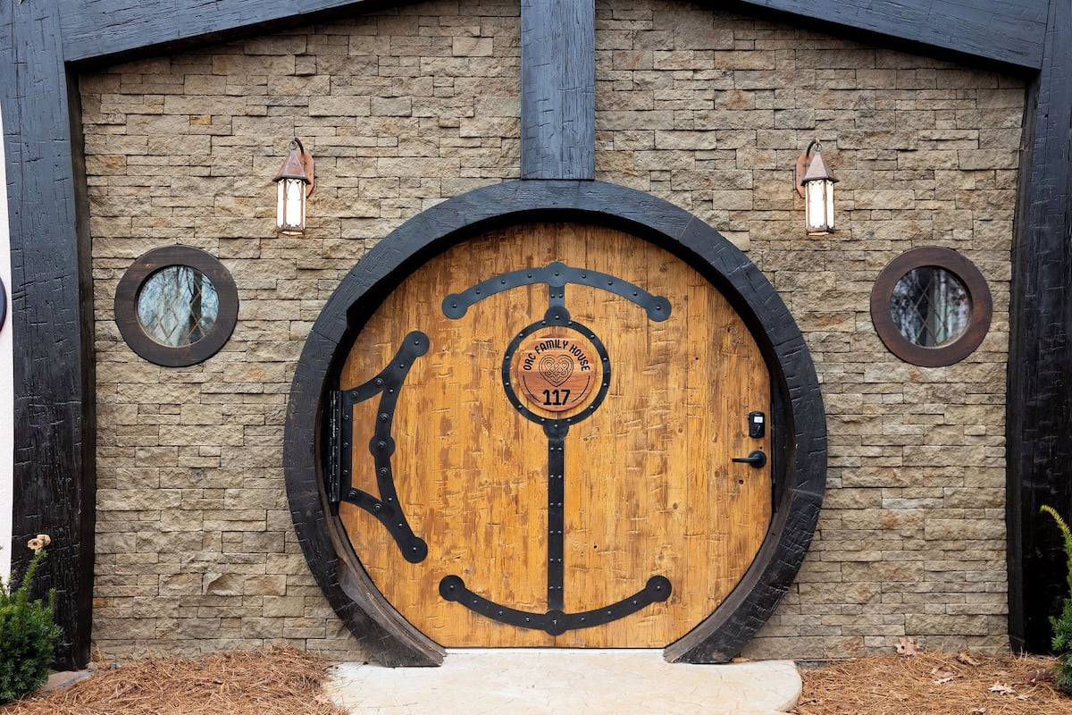 A wooden door with a circular design, a stone wall, and two lantern-style lights.