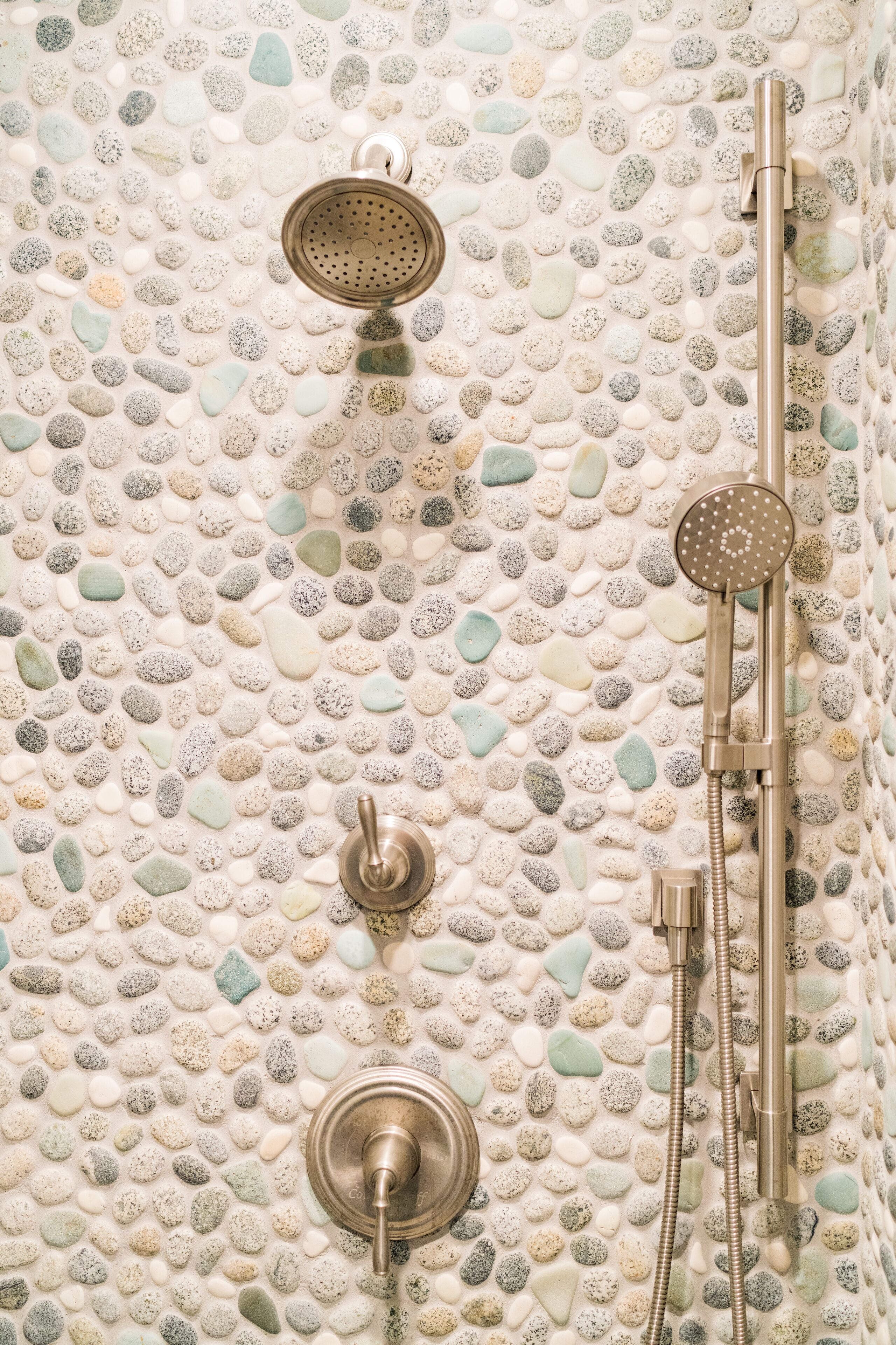 A shower with a pebble-patterned wall, a handheld showerhead, and a wall-mounted control.