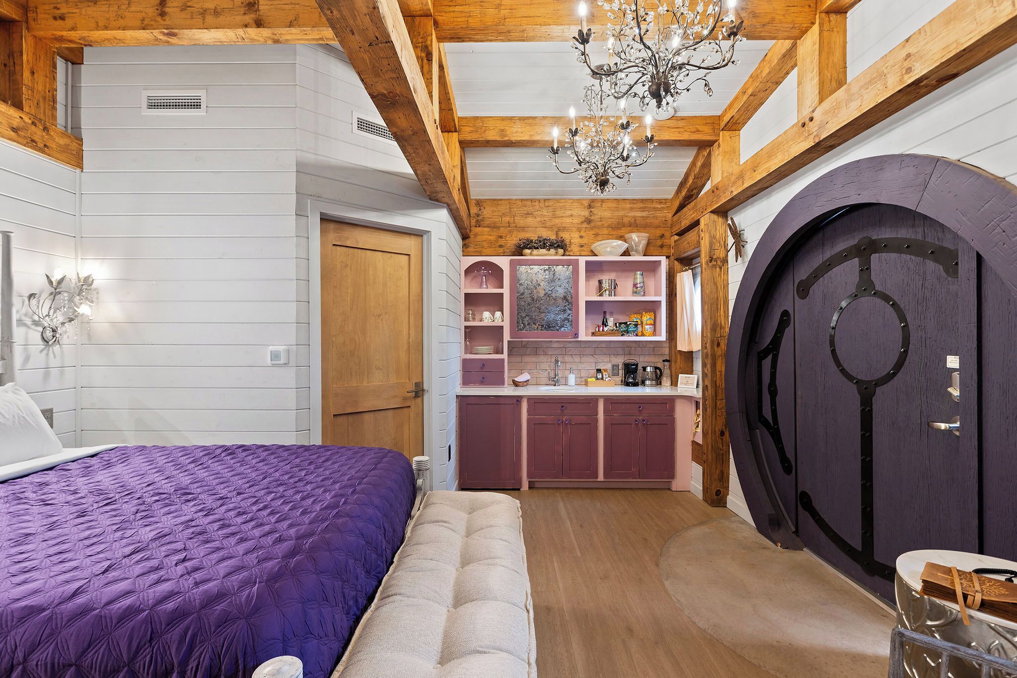 Quarto com uma cama grande, um banquinho e teto de madeira.