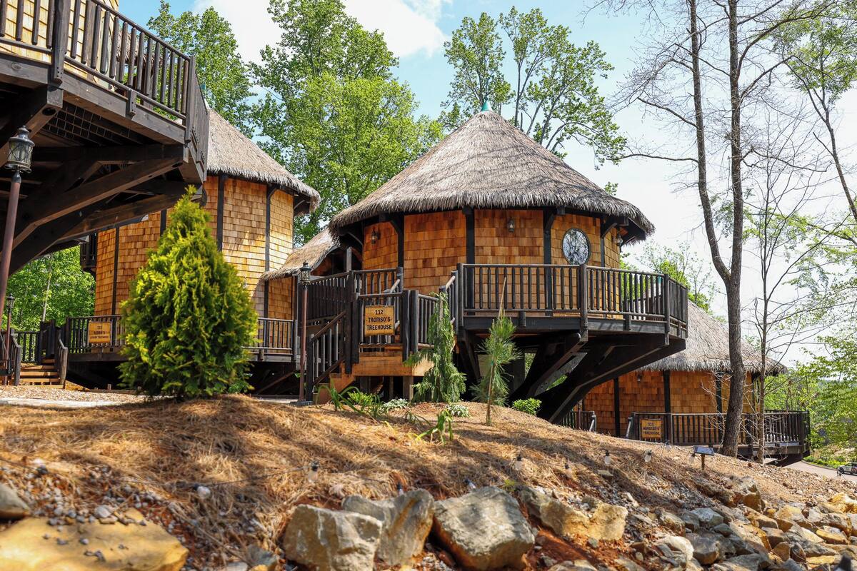 A treehouse with a thatched roof, wooden exterior, and a balcony.