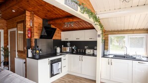 A modern kitchen with white cabinets, a black countertop, and a wooden ceiling. - Ty Coed - 63 (Blaenau Ffestiniog)