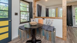 A room with a wooden bench seating area, a round table, and a door with a yellow stripe.