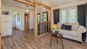 A spacious living area with a wooden ceiling, a sofa, a small table, and a view of the outdoors through large windows.