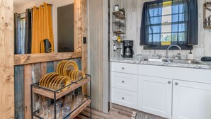 A kitchen with white cabinets, a granite countertop, a coffee maker, and a window with curtains.