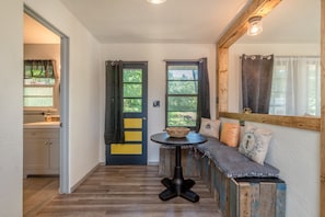 Un couloir avec un banc en bois, une petite table ronde sur laquelle se trouve un bol, et une porte avec des rideaux.