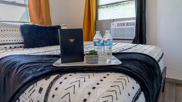 A neatly made bed with a patterned bedspread, a laptop, two water bottles, and a small potted plant on a tray.