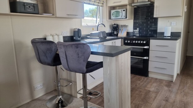 A modern kitchen with a central island, bar stools, a microwave, a stove, and a coffee maker. - 3 Bedroom Static Caravan, Hoburne Devon Bay (Paignton)