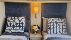 A cozy bedroom with two beds, a nightstand with a lamp, and a decorative wall piece above the beds. - 3 Bedroom Static Caravan, Hoburne Devon Bay (Paignton)