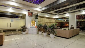 A modern interior with a reception desk, potted plants, a sofa, and a dining area. - Treebo Nearmi Bell House (Gurugram)