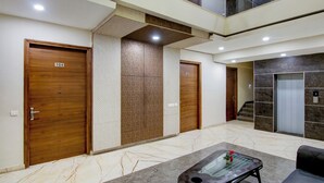 A hotel lobby with three wooden doors, a marble floor, and a glass-top table with a vase. - Treebo Nearmi Bell House (Gurugram)