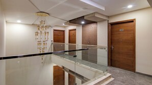 A modern hotel lobby with a glass railing, wooden doors, and a decorative hanging light fixture. - Treebo Nearmi Bell House (Gurugram)