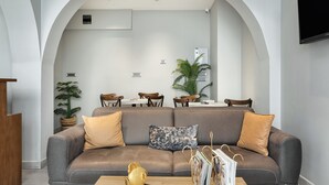 A modern living room with a grey sofa, two wooden chairs, a coffee table, and a TV mounted on the wall. - Galata Rasso Boutique Hotel (Istanbul)