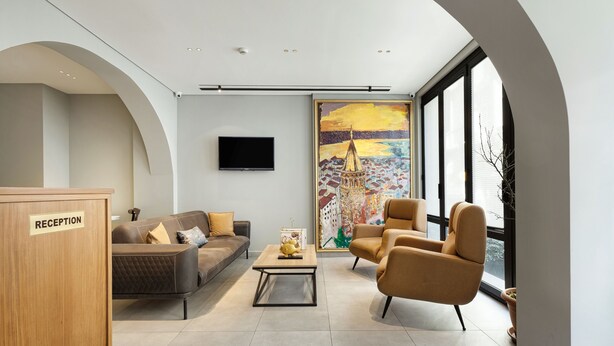 A modern reception area with a reception desk, a sofa, a coffee table, and a large window with a painting. - Galata Rasso Boutique Hotel (Istanbul)